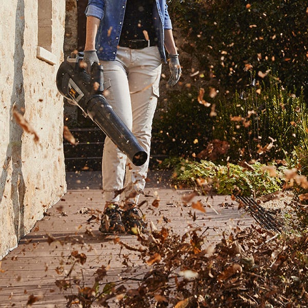 Woman using Alpina 40V battery leaf blower to clean pathway from leaves